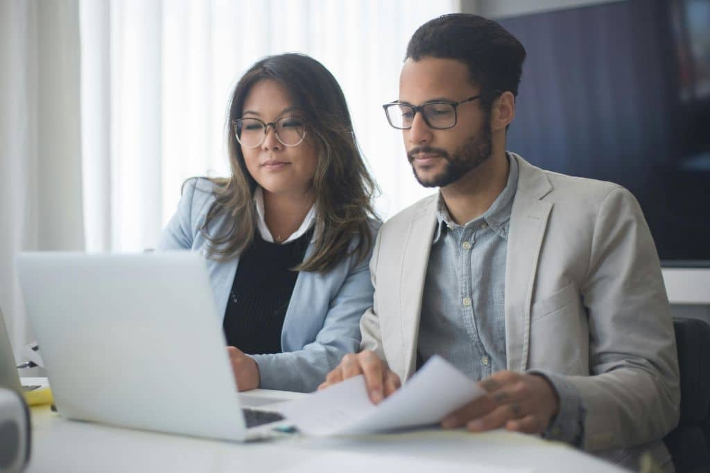 Article CIP-KYC - Un homme et une femme, consultent ensemble un ordinateur portable tout en tenant des documents