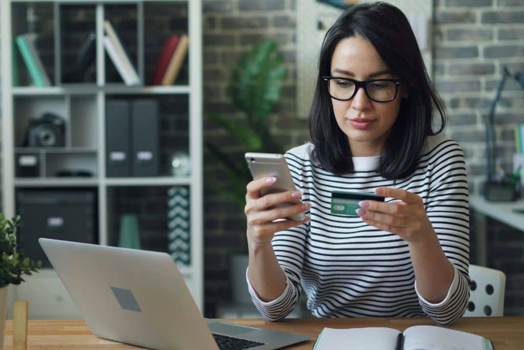 Article compte bancaire en agence ou en ligne - Une entrepreneure effectue une transaction en ligne sur son smartphone en tenant sa carte de crédit