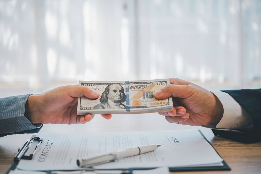 Article Crédit et prêts US - Deux mains échangent un paquet de billets de dollars au-dessus d’un contrat posé sur la table