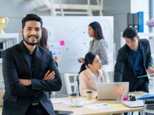 Article LLC vs IBC Seychelles - Un entrepreneur debout au premier plan et son équipe travaille en arrière-plan dans un environnement dynamique et collaboratif