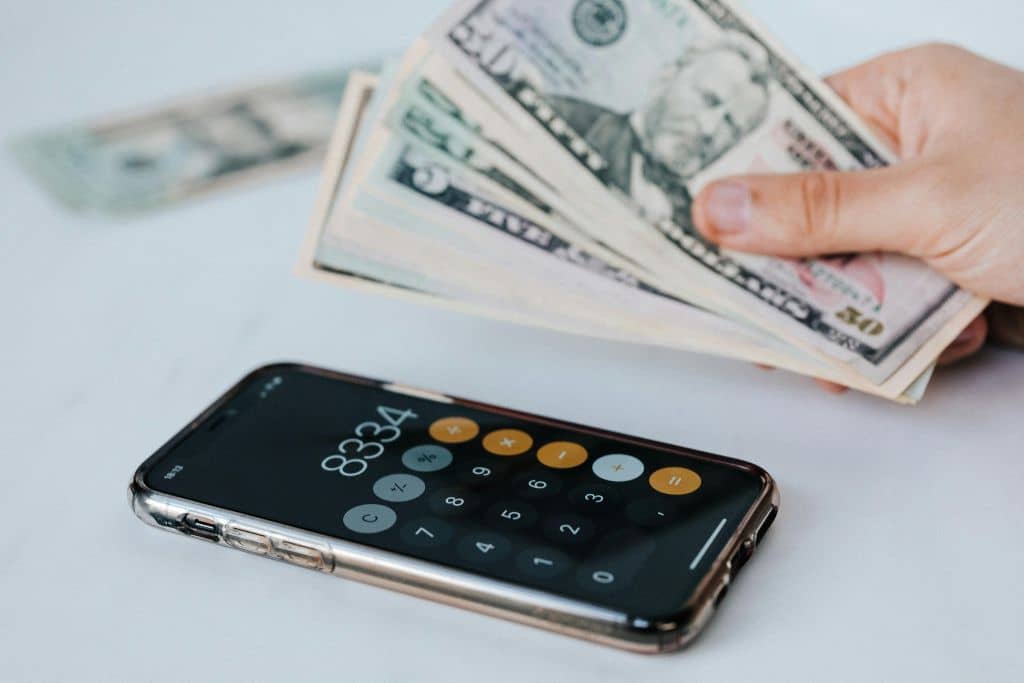 LLC vs Stiftung du Liechtenstein - Un smartphone ouvert sur la calculatrice, posé à côté d'une main tenant des dollars américains