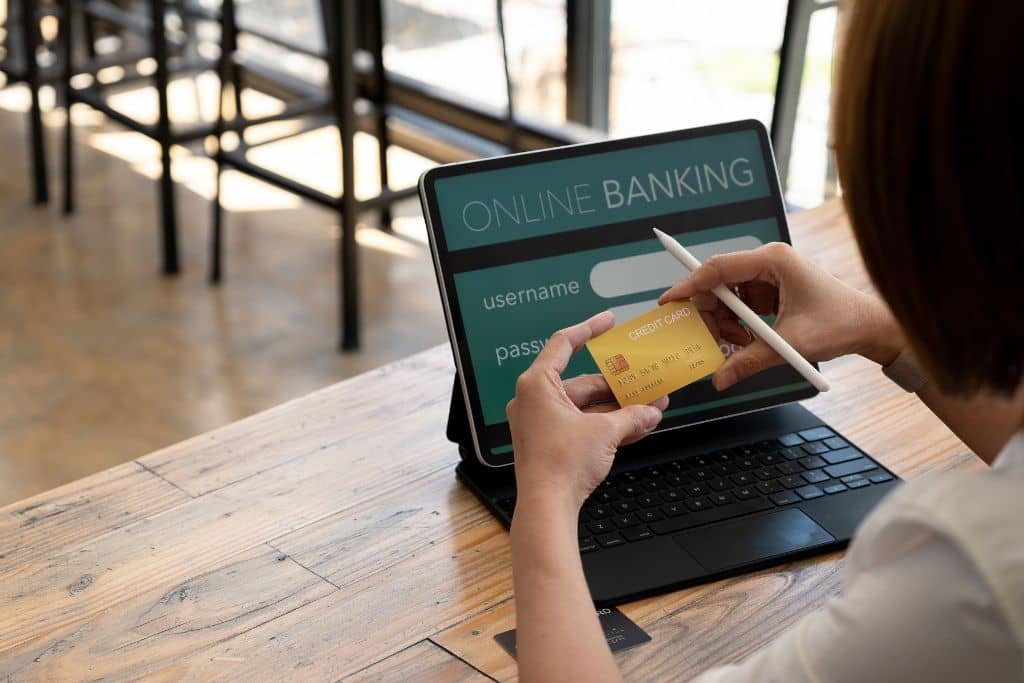 Article Système bancaire américain - Une main tient une carte de crédit devant un ordinateur affichant une interface d’online banking